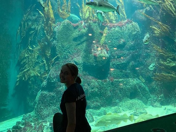 Filiz sitzt vor einem großem Aquarium und lächelt in die Kamera. 