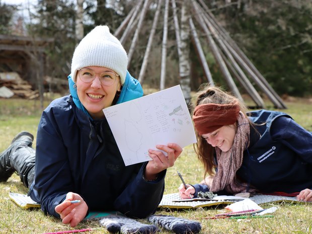 Person hält auf Bauch liegend ein Blatt Papier in die Luft.