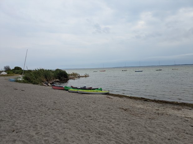 Blick auf das Meer vom Sandstrand aus, an der Wasserkante liegen ein paar Kanus