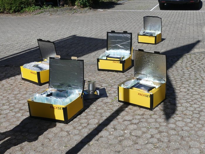 Fünf gelbe, aus gelben Postkartons gebaute Solarbacköfen, stehen zur Sonne ausgerichtet auf dem Boden