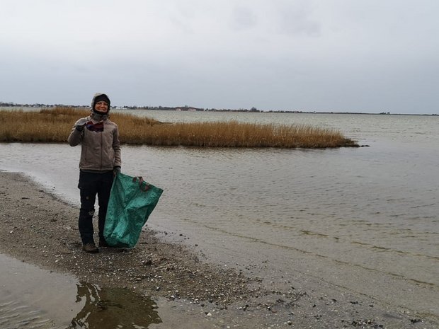 Auf einer Steinfläche umgeben von flachem Wasser sammelt Sina Müll mit einem großen Müllbeutel.