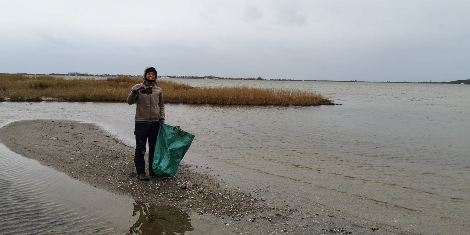 Auf einer Steinfläche umgeben von flachem Wasser sammelt Sina Müll mit einem großen Müllbeutel.