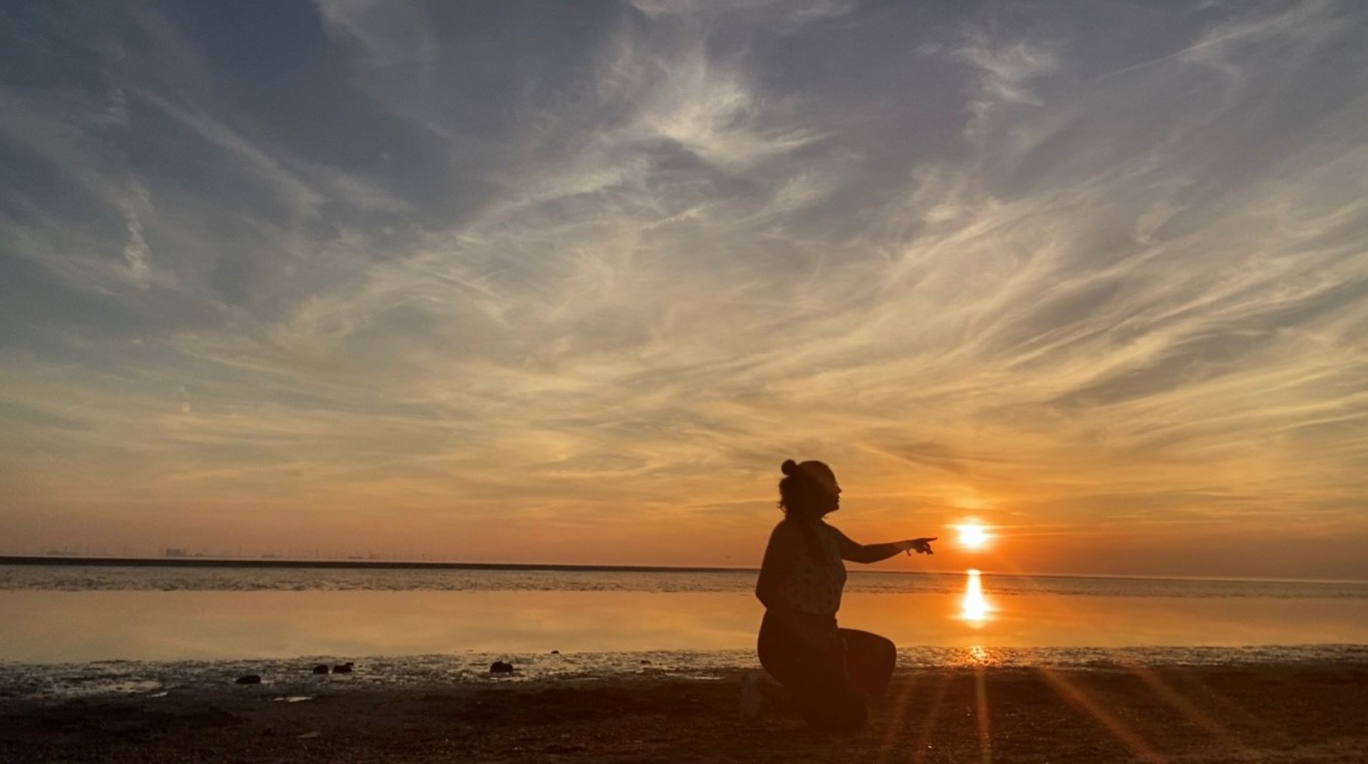 Der Schattenriss einer Person vor dem Sonnenuntergang im Wattenmeer.
