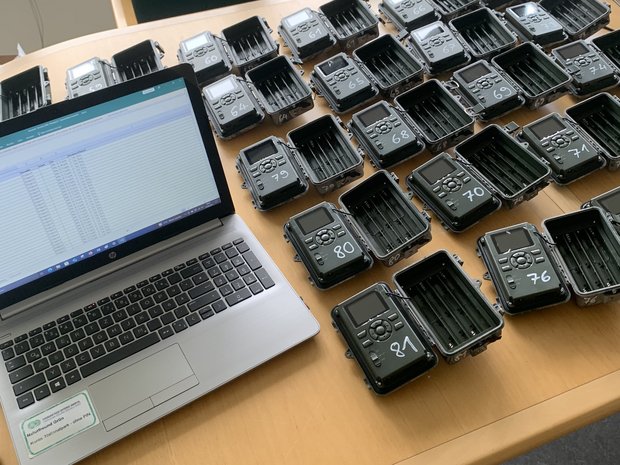 Auf einem Tisch steht ein Laptop, daneben liegen viele Wildtierkameras