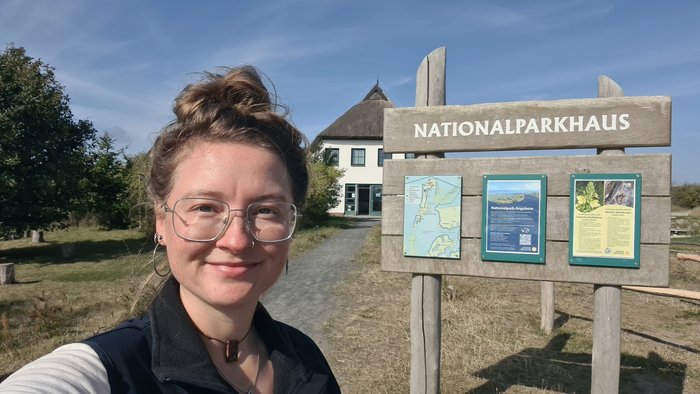 Minouschka stehet vor einem Holzschild mit der Aufschrift: Nationalparkhaus.