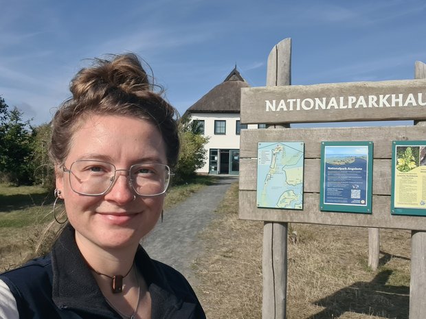 Minouschka stehet vor einem Holzschild mit der Aufschrift: Nationalparkhaus.