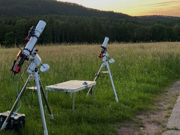 Zwei nach oben gerichtete Teleskope stehen bei Sonnenuntergang auf einer Wiese. 