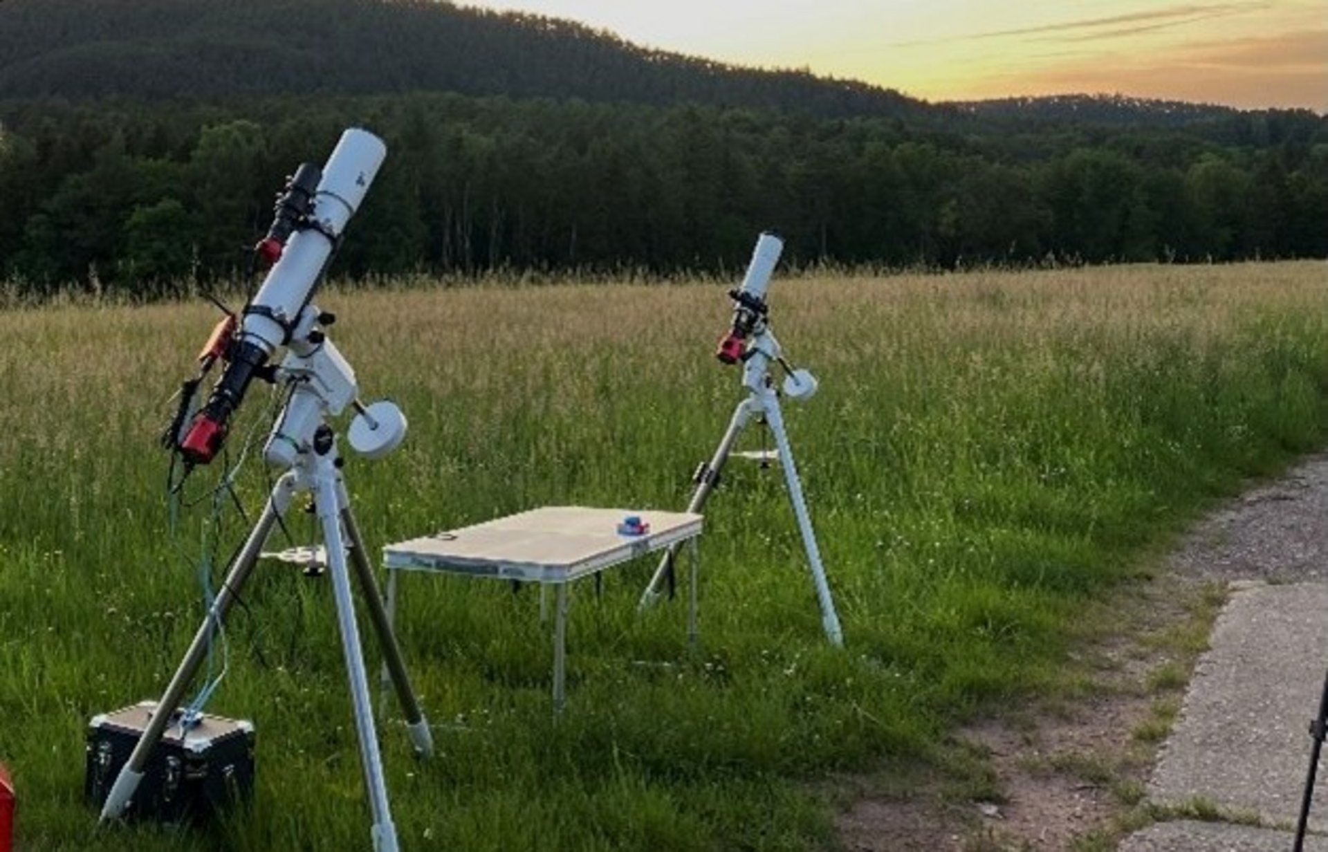 Zwei nach oben gerichtete Teleskope stehen bei Sonnenuntergang auf einer Wiese. 