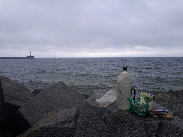 Blick auf Plastikmüll welcher auf einer Steinbucht vor dem offenen Meer platziert ist. 
